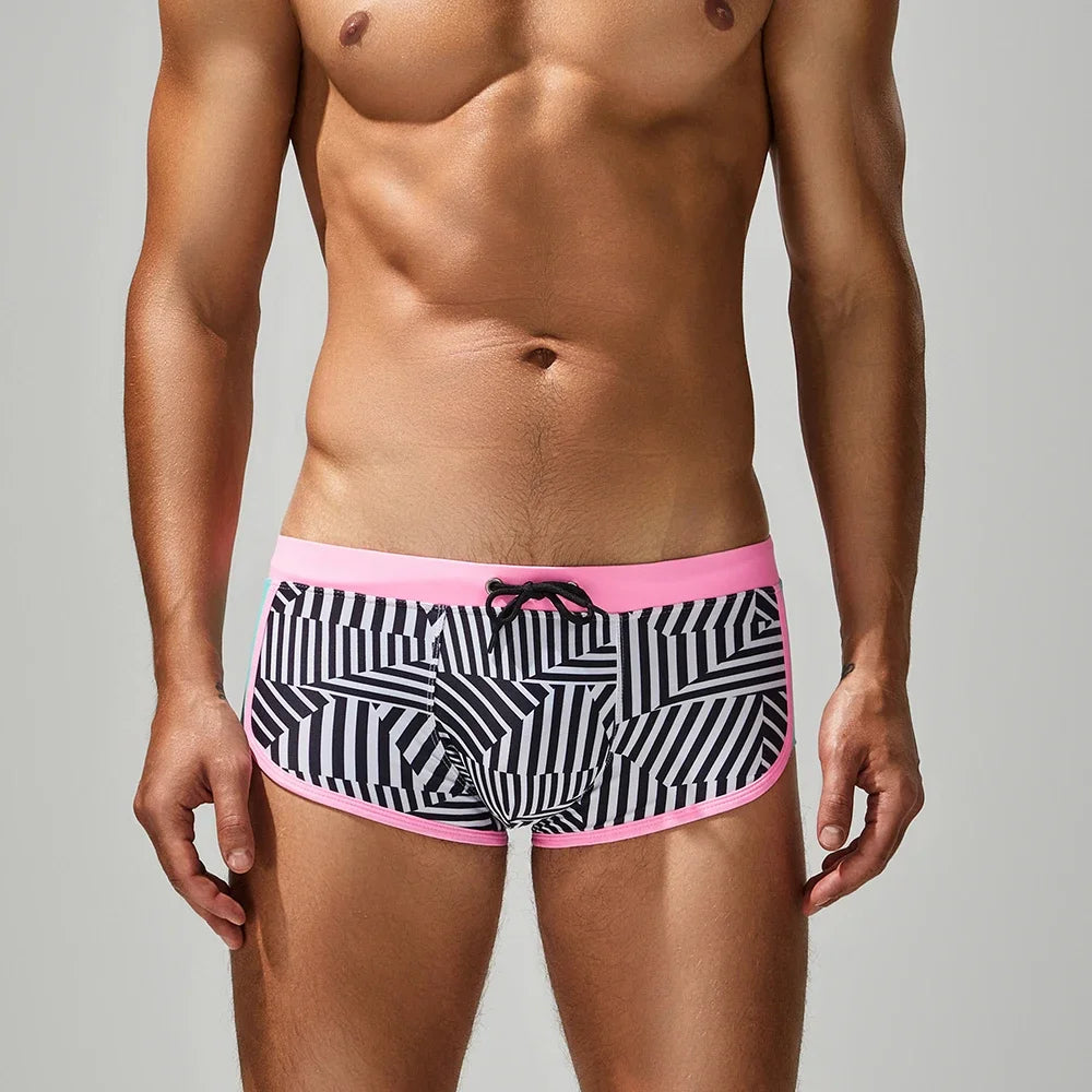 Man wearing black and white patterned underwear with pink waistband on a gray background