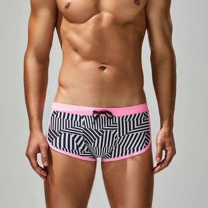 Man wearing black and white patterned underwear with pink waistband on a gray background
