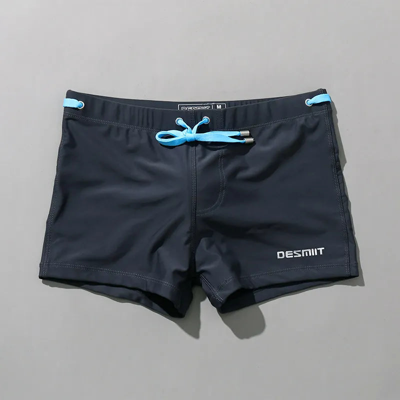 Black swim shorts with blue drawstring and DESMIIT branding on a gray background