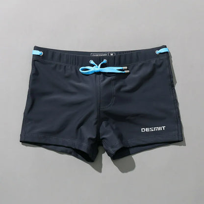 Black swim shorts with blue drawstring and DESMIIT branding on a gray background