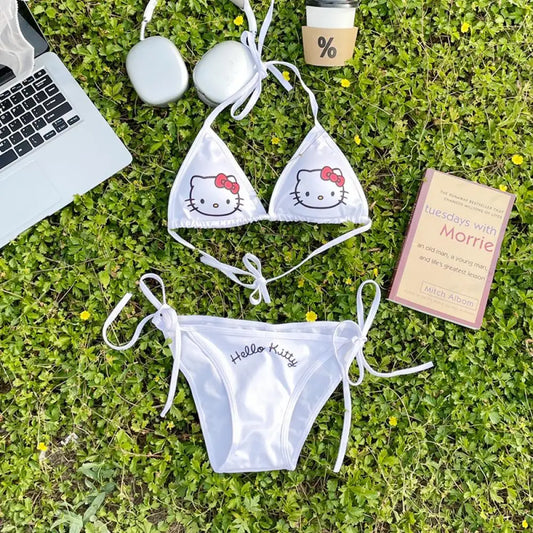 White Hello Kitty bikini set on grass with a laptop, phone, and book.