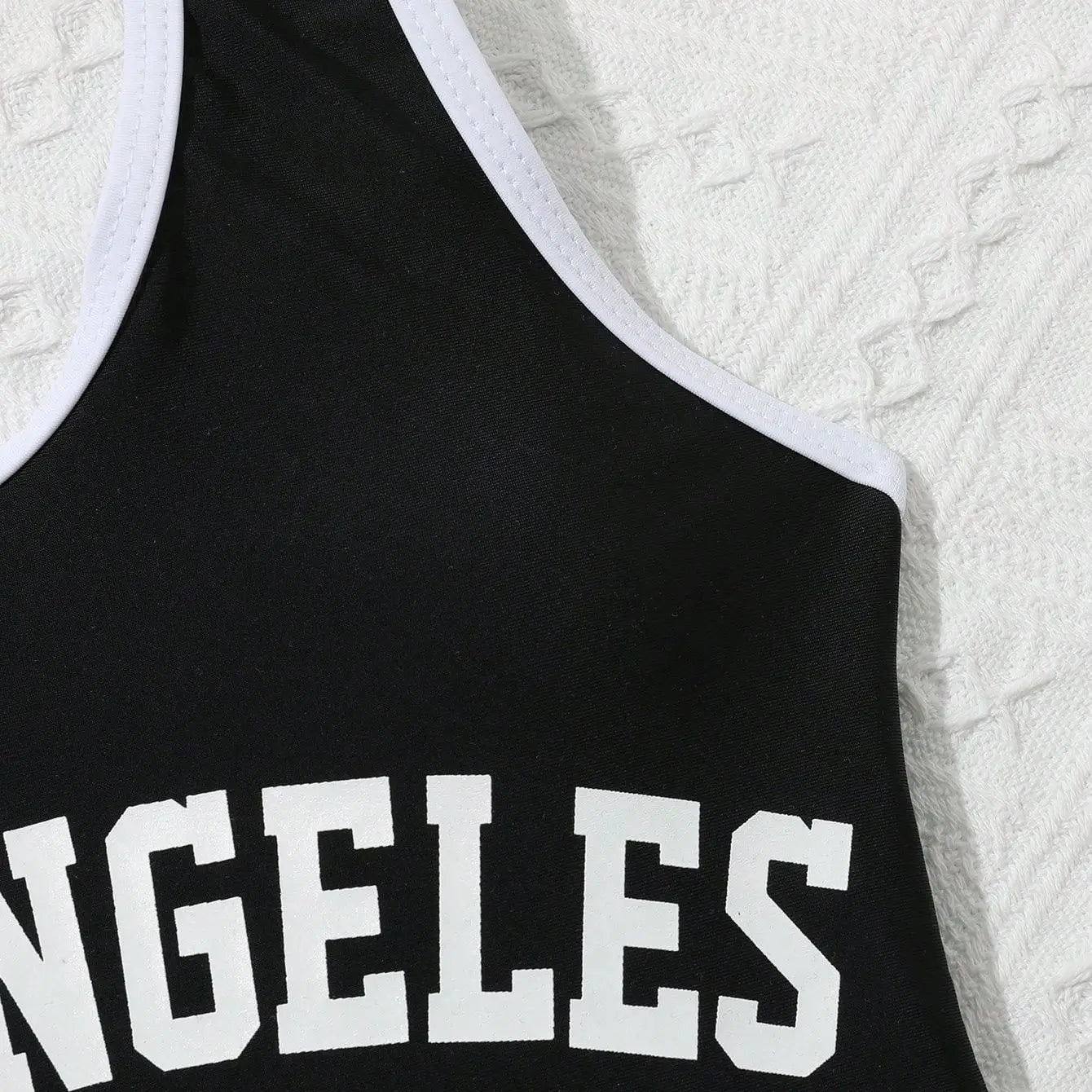 Black tank top with 'ANGELES' printed on it against a textured white background