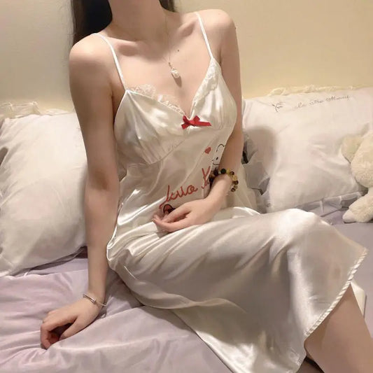 Woman in a white nightgown sitting on a bed with white pillows and a teddy bear.