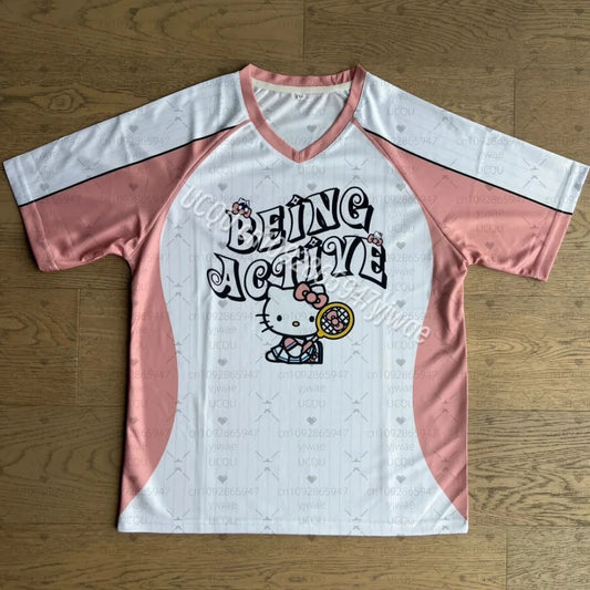White and pink baseball shirt with 'Being Active' text and Hello Kitty graphic on a wooden surface