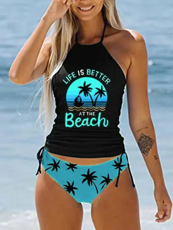 Woman wearing a black and blue bikini with 'Life is Better at the Beach' text and palm tree design.