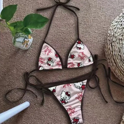 Hello Kitty bikini set on a textured surface with a plant and straw hat in the background