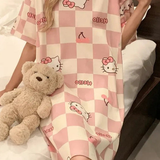 Person wearing a pink checkered nightgown with cartoon characters, sitting on a bed with a teddy bear.