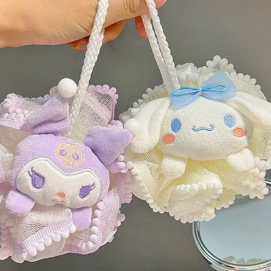 Two small kitty bath sponge plush toys, one purple and one white with a bow, held by a hand against a neutral background.