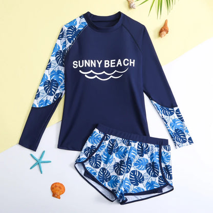 Navy blue and blue leaf-patterned children's swimsuit with 'Sunny Beach' text on a yellow background.