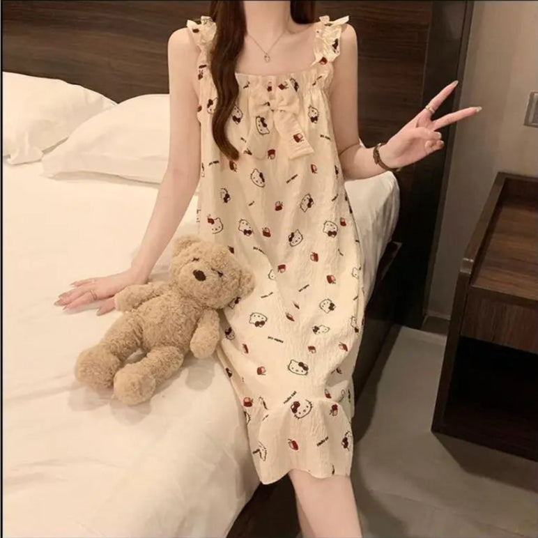 Woman in a patterned dress sitting on a bed with a teddy bear, making a peace sign.