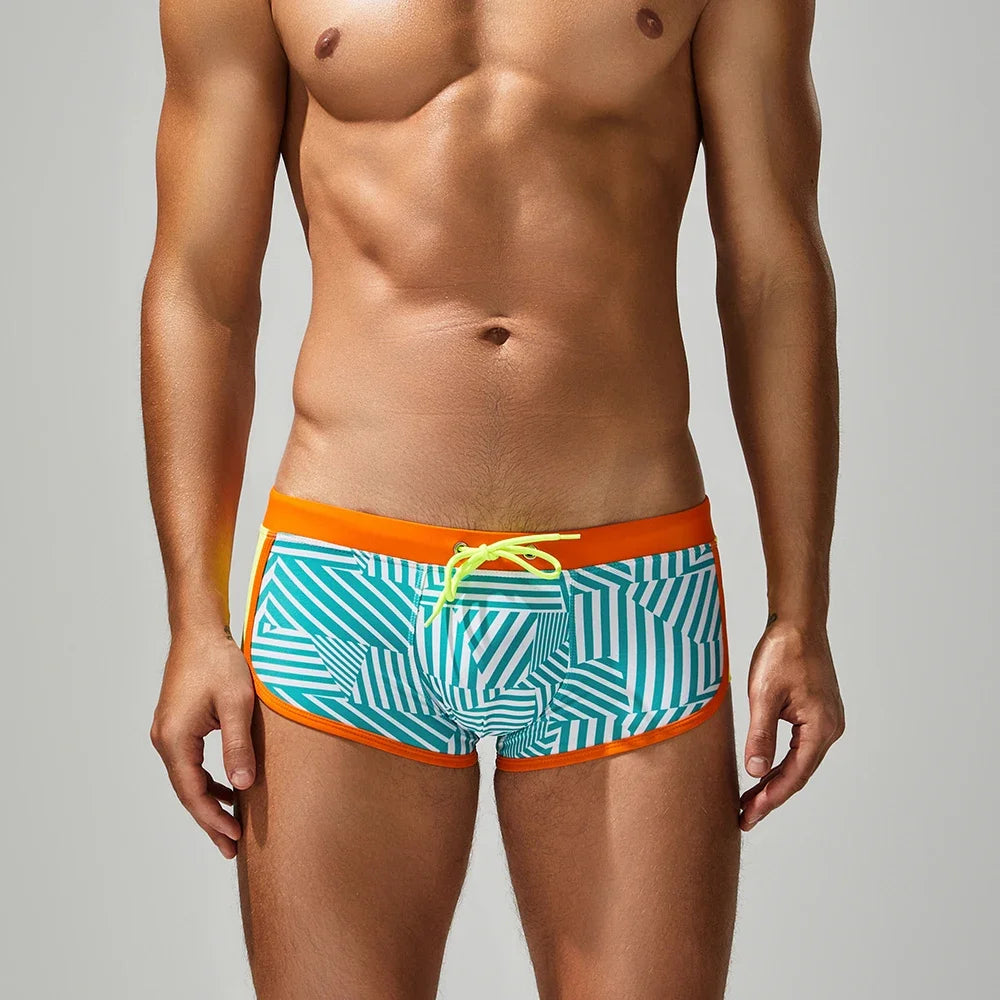 Man wearing a patterned swim trunk with orange waistband on a gray background