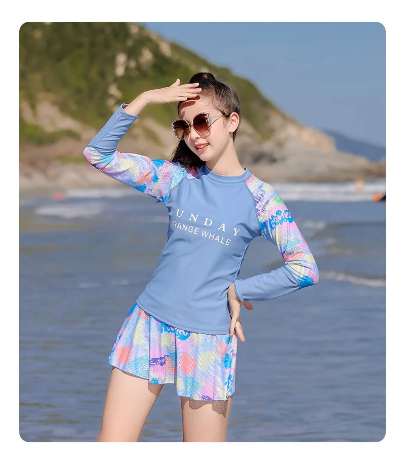 Girl in colorful long-sleeve rash guard and shorts standing on a beach.