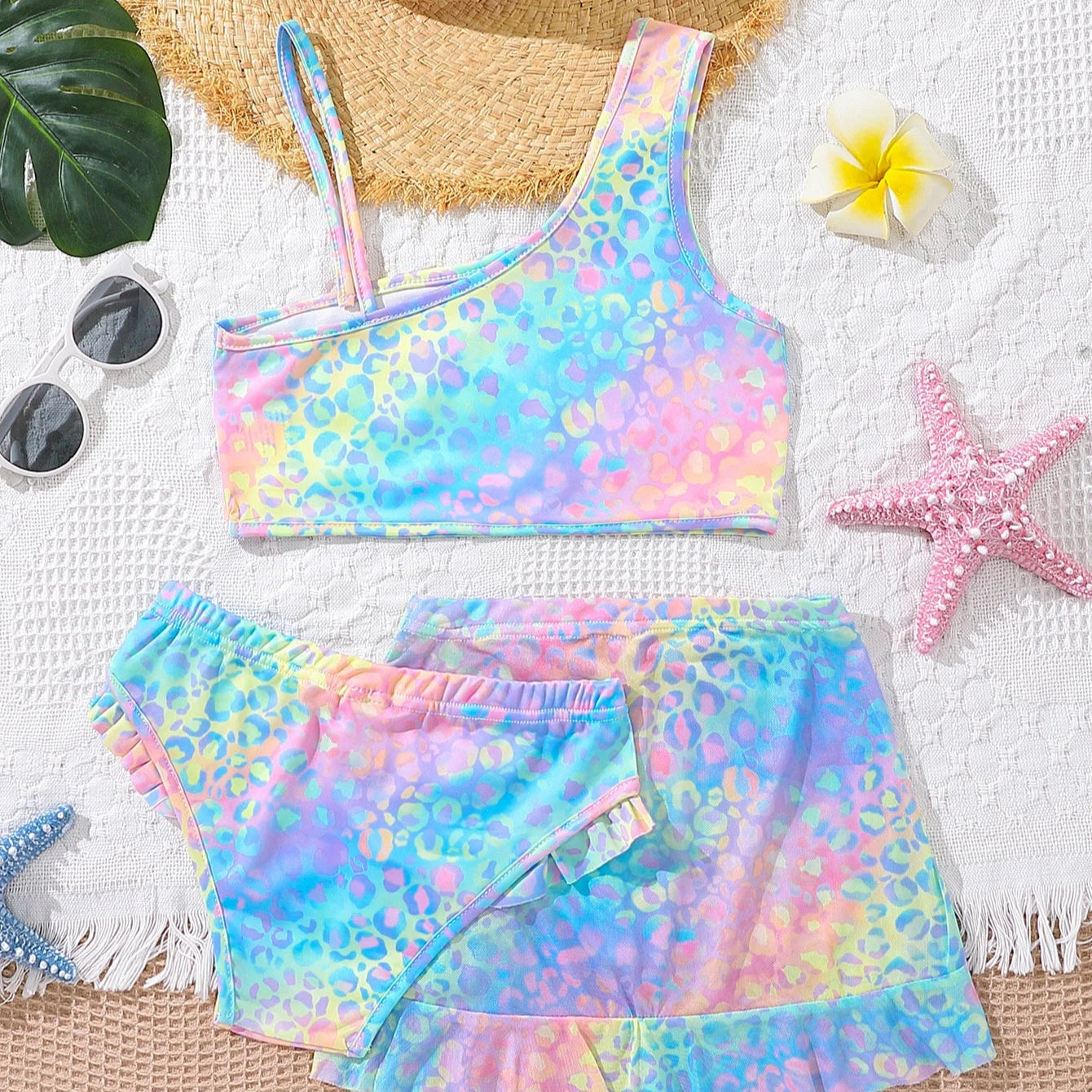 Colorful tie-dye swimsuit with matching shorts on a textured surface with beach accessories.