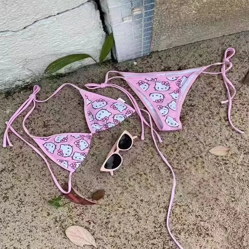 Pink Hello Kitty bikini set with sunglasses on a concrete surface.