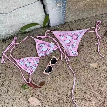 Pink Hello Kitty bikini set with sunglasses on a concrete surface.