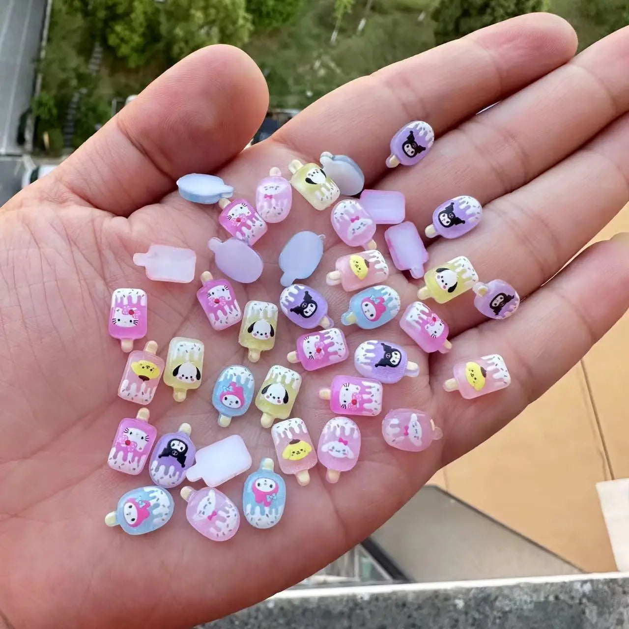 Hand holding small colorful resin charms with various designs.