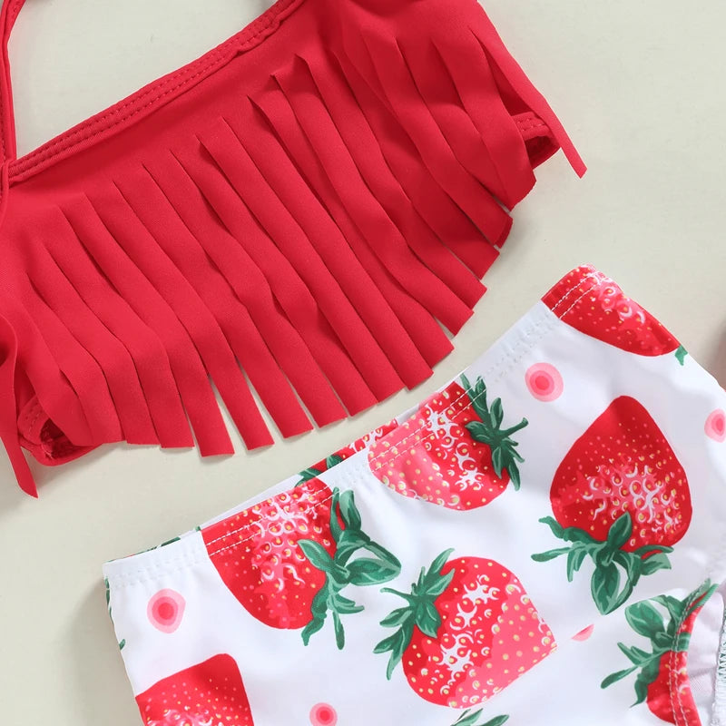 Red bikini top with fringe details and strawberry-patterned shorts on a light background