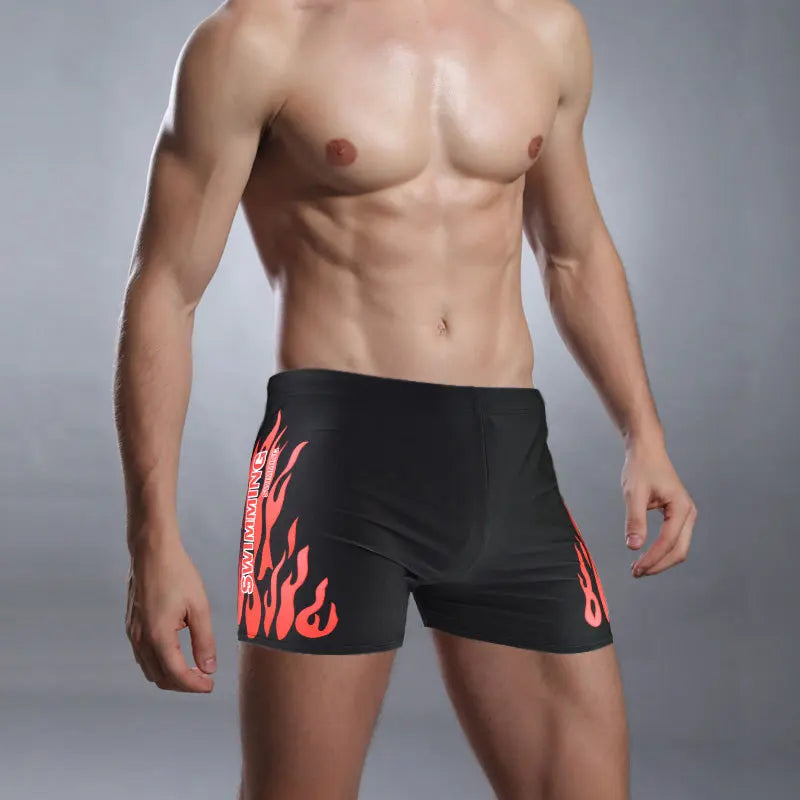 Man wearing black swim shorts with red flame design on a gray background