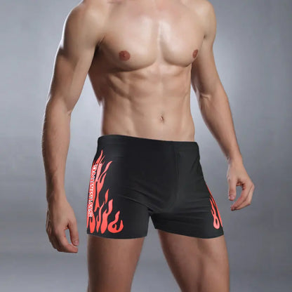 Man wearing black swim shorts with red flame design on a gray background