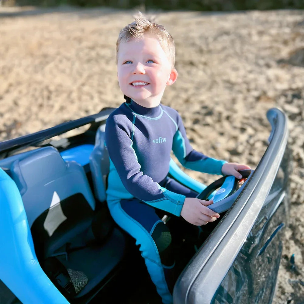 Child in a wetsuit sitting in a small vehicle on a beach