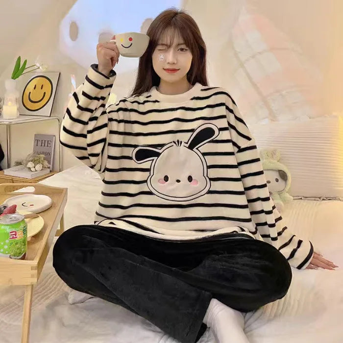 Person wearing a black and white striped sweater with a cartoon design, sitting on a bed.