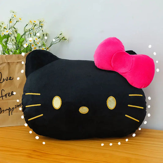 Black cat-shaped pillow with a pink bow on a wooden surface with flowers and a bag in the background.