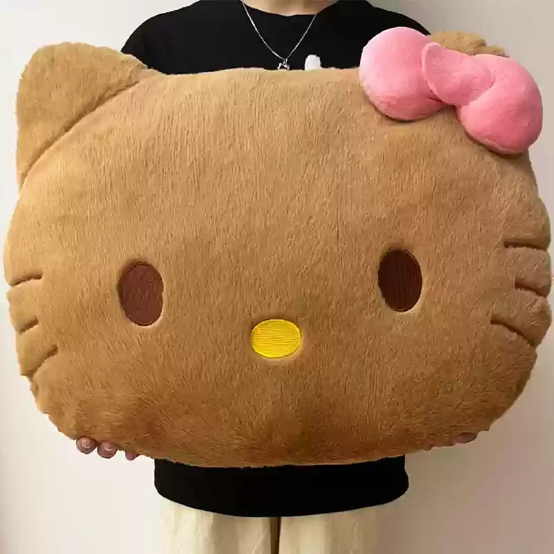 Large plush pillow shaped like a cat's face with a pink bow held by a person.
