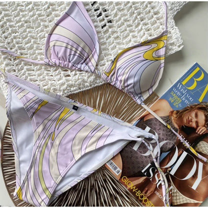 Colorful patterned bikini set on a textured surface with a magazine underneath.
