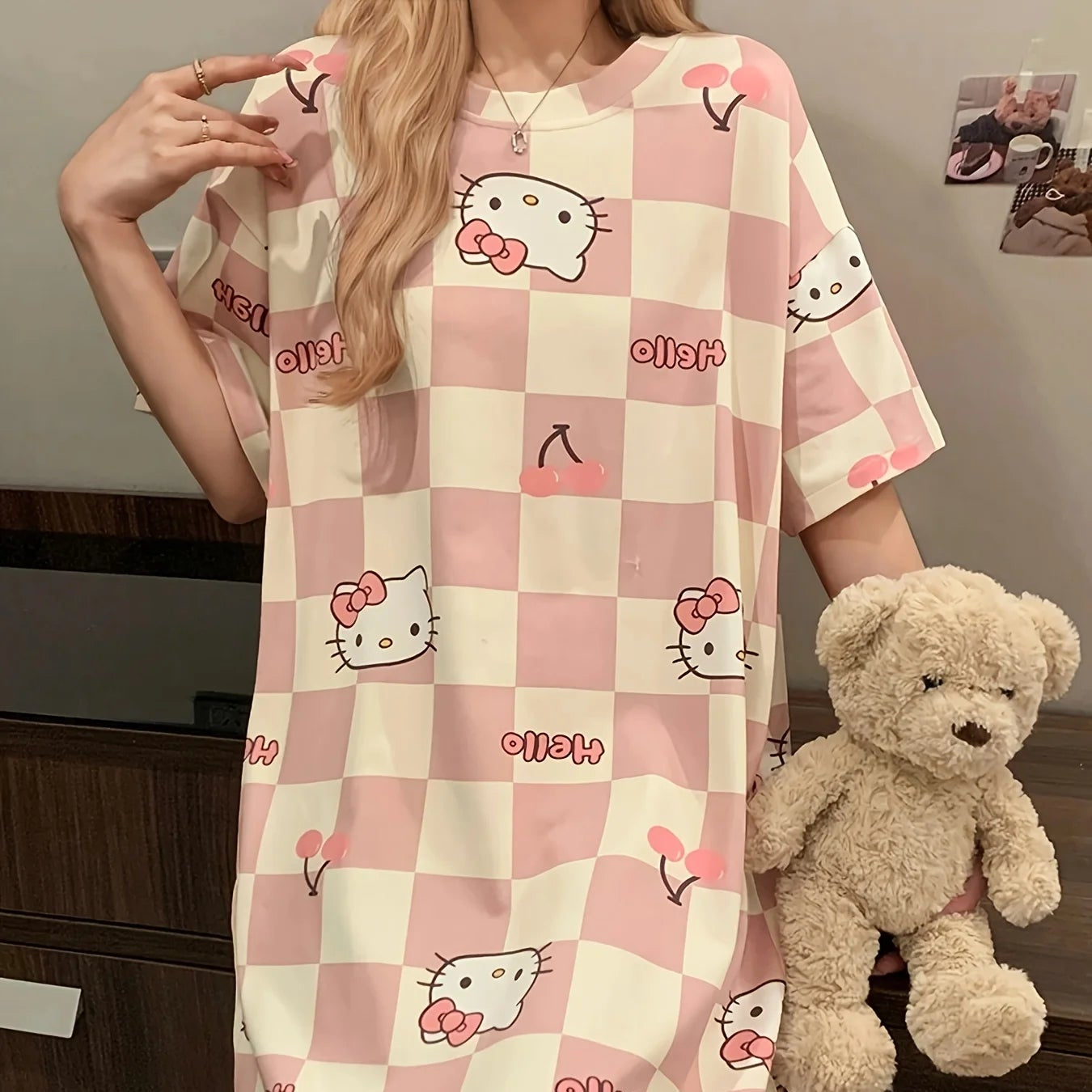 Person wearing a pink and white checkered dress with Hello Kitty designs, holding a teddy bear.