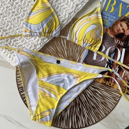 Yellow and white patterned bikini set on a textured surface with a magazine underneath.