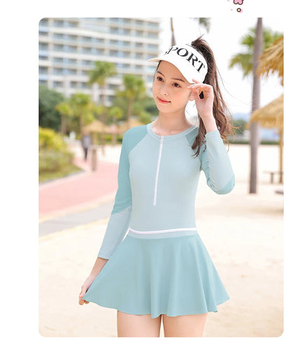 Woman wearing a light blue swimsuit with a skirt and white cap in a beach setting
