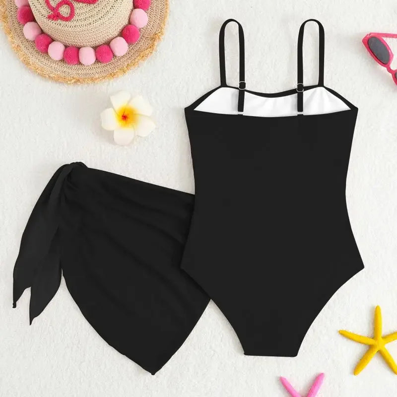 Black swimsuit with a matching black sarong on a white background with beach accessories.