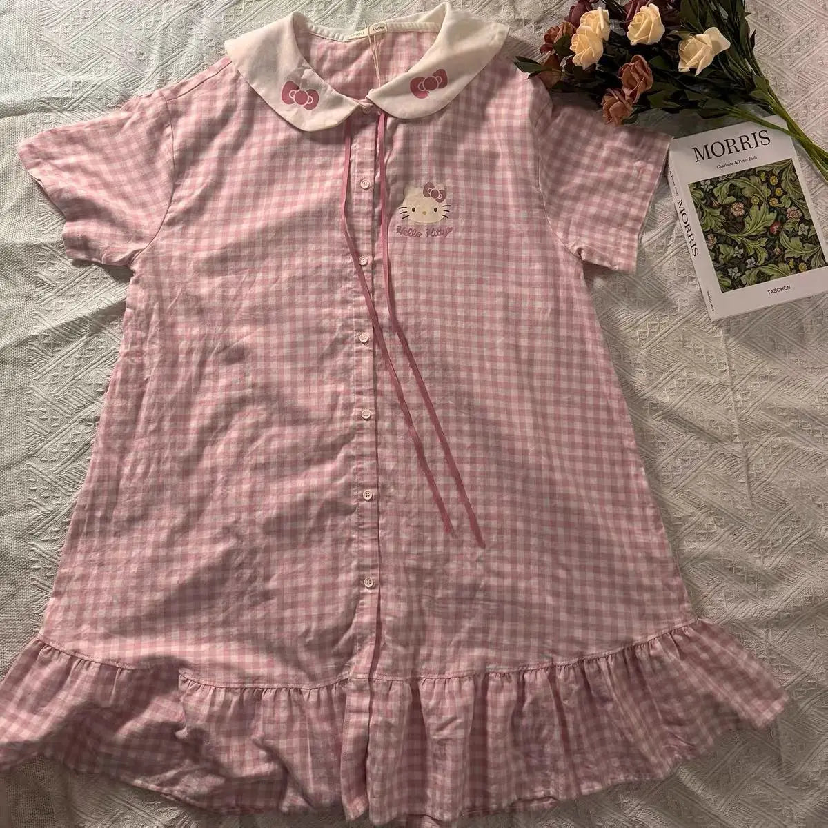 Pink checkered dress with Hello Kitty design on a bed with flowers and a magazine.