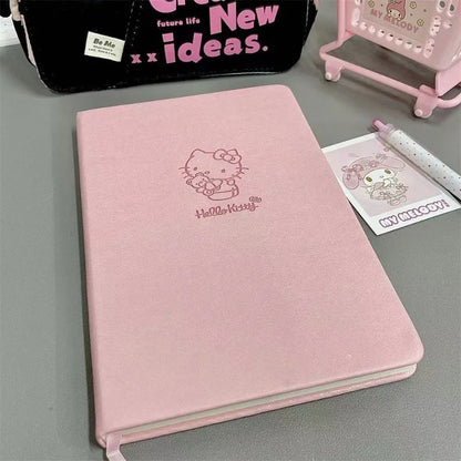Pink notebook with Hello Kitty design on a gray surface, surrounded by stationery items.