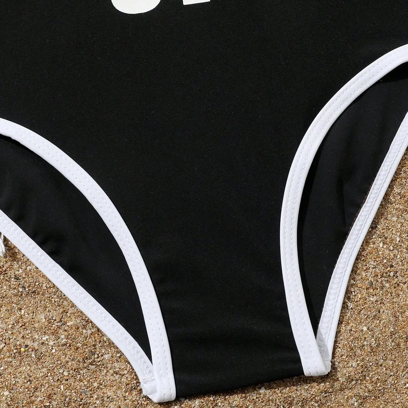 Black swimsuit with white trim on a sandy surface
