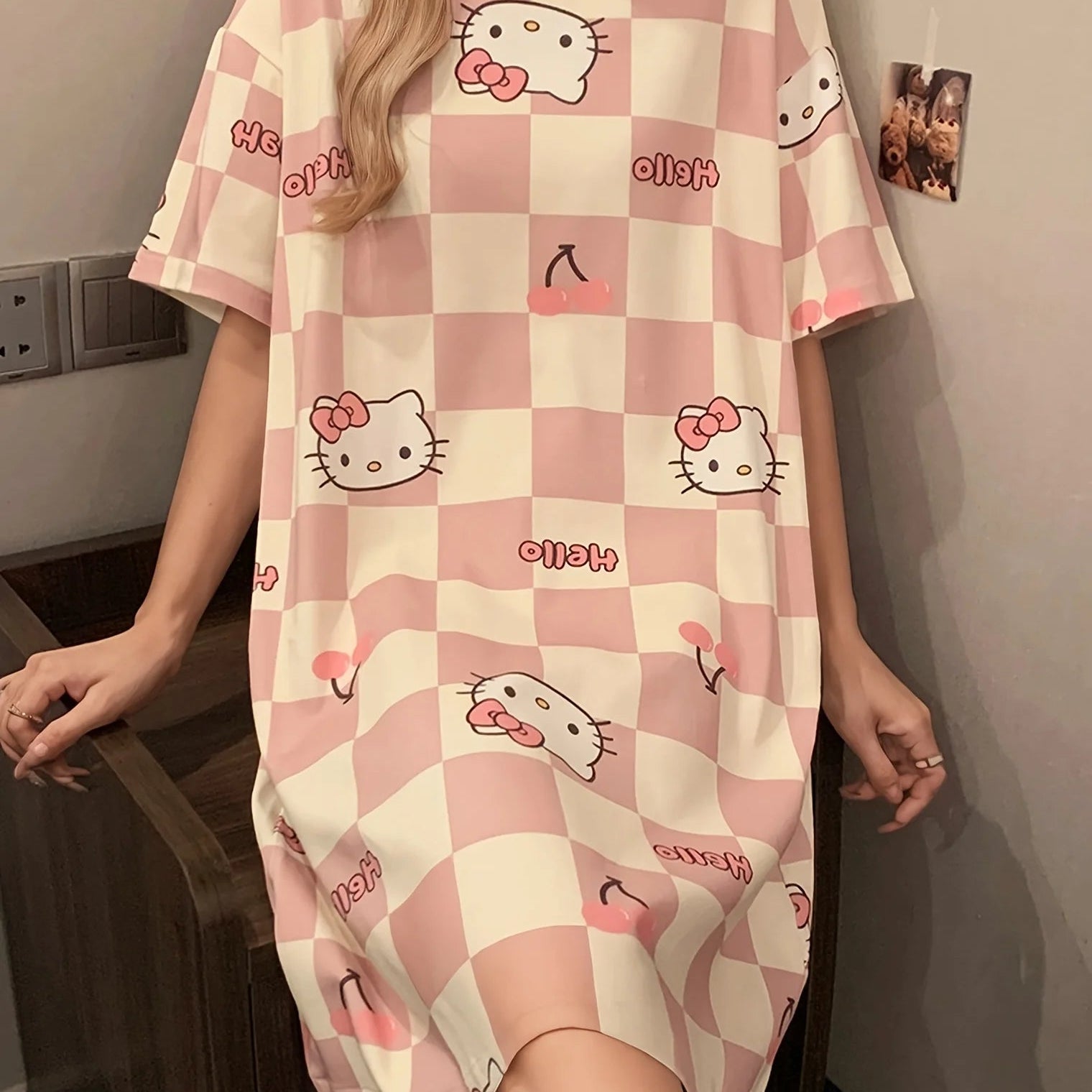 Person wearing a checkered dress with Hello Kitty designs in a room.