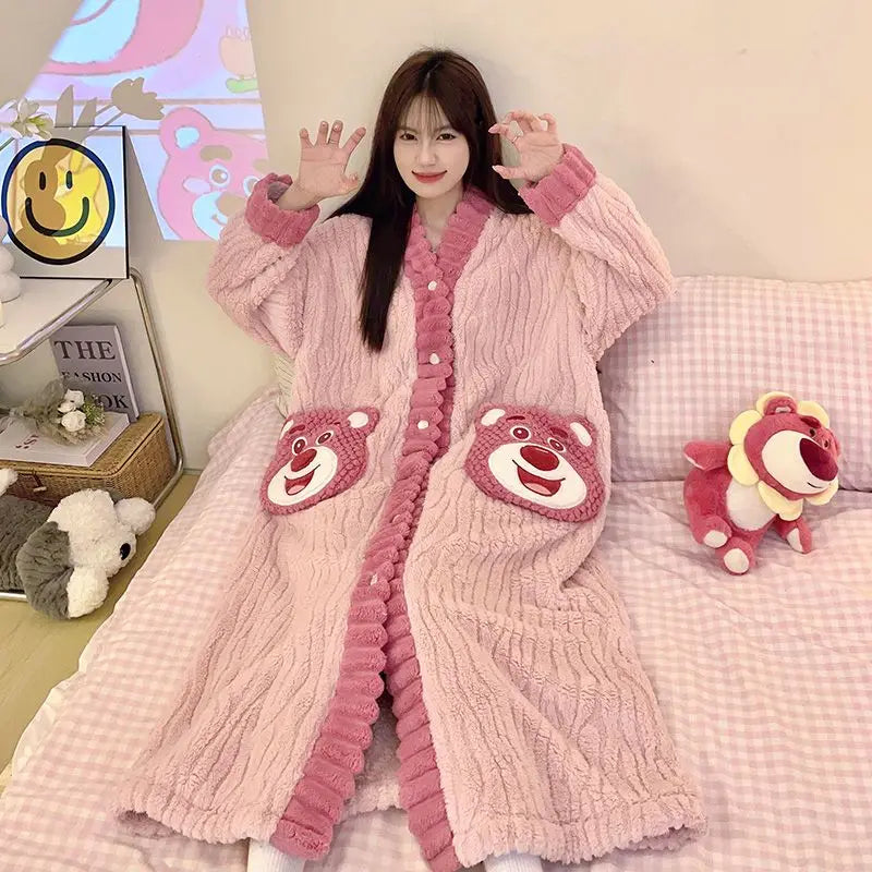 Person wearing a pink plush robe with bear face pockets, sitting on a bed.