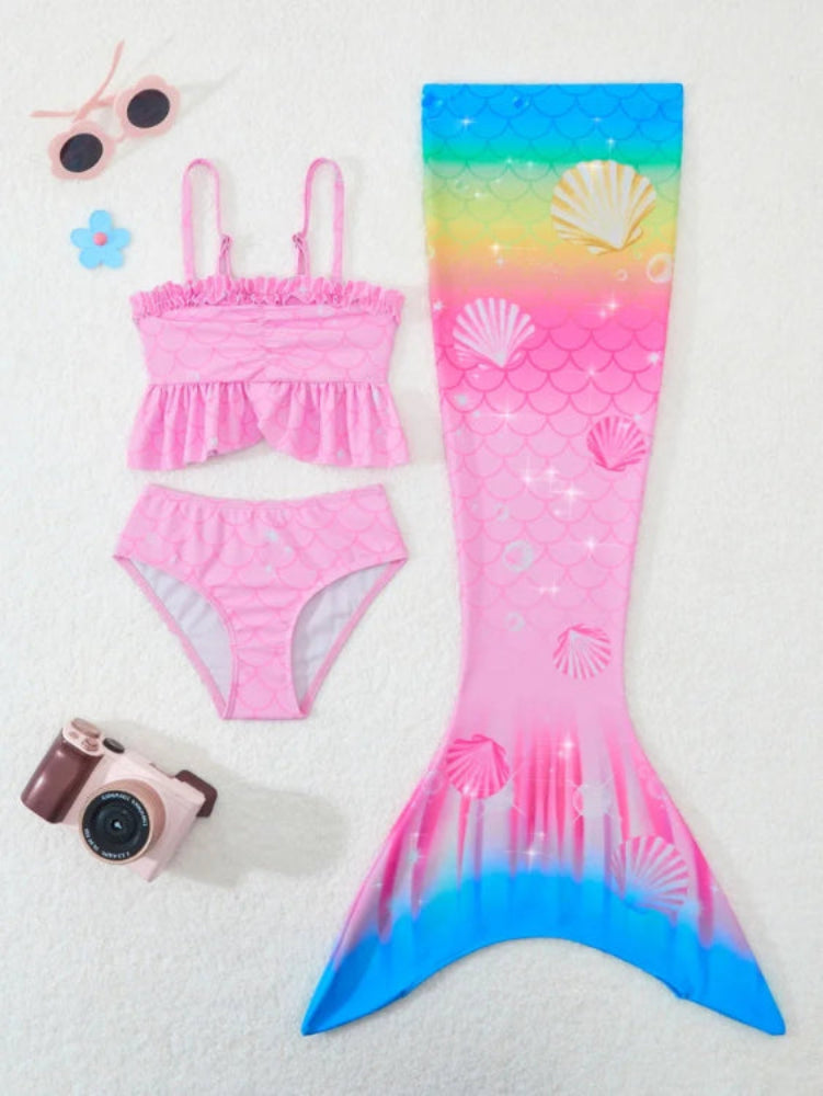 Pink mermaid tail swimsuit with shell pattern, sunglasses, camera, and flower on a white background