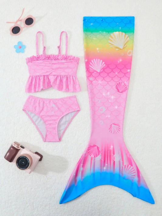 Pink mermaid tail swimsuit with shell pattern, sunglasses, camera, and flower on a white background
