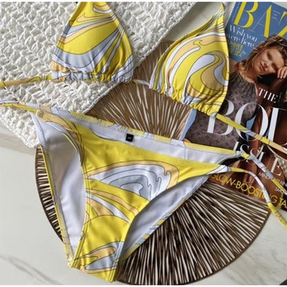 Yellow and white patterned bikini set on a textured surface with a magazine underneath.