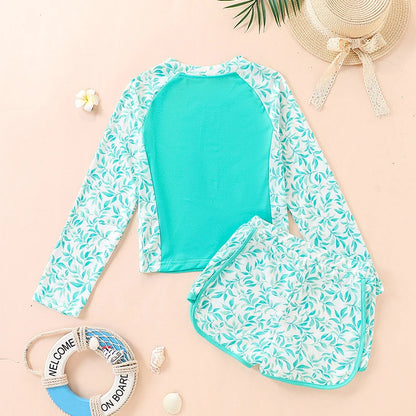 Teal and white leaf-patterned swimsuit with matching cover-up on a beige background.