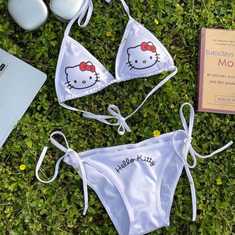 White Hello Kitty bikini set on grass with a book and bottle in the background