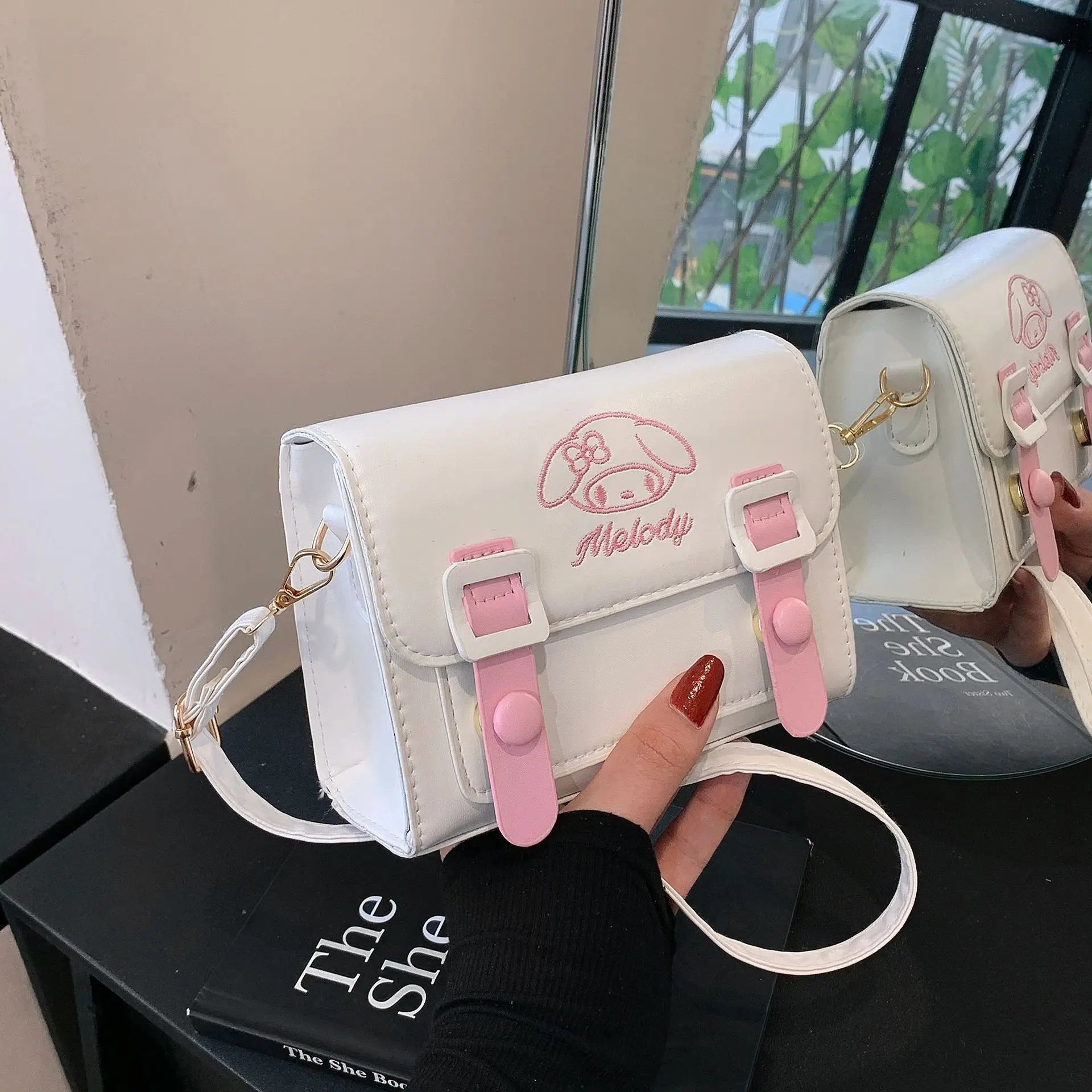 White and pink bag with 'Melody' branding held by a hand on a black surface.