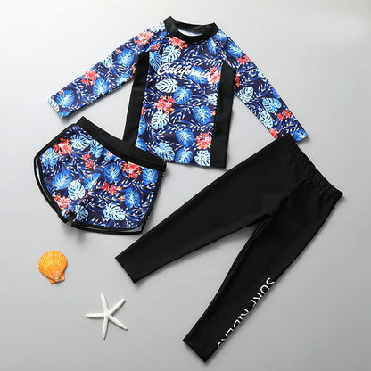 Children's floral rash guard and black swim pants on a gray background with a shell and starfish.