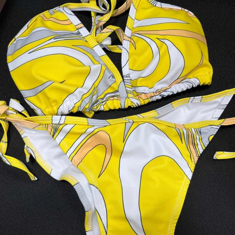 Yellow and white patterned bikini set on a textured surface with a magazine underneath.