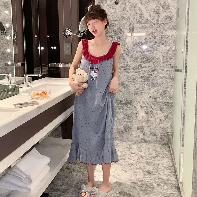 Child in a blue dress with red accents standing in a bathroom holding a teddy bear.