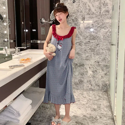 Child in a blue dress with red accents standing in a bathroom holding a teddy bear.