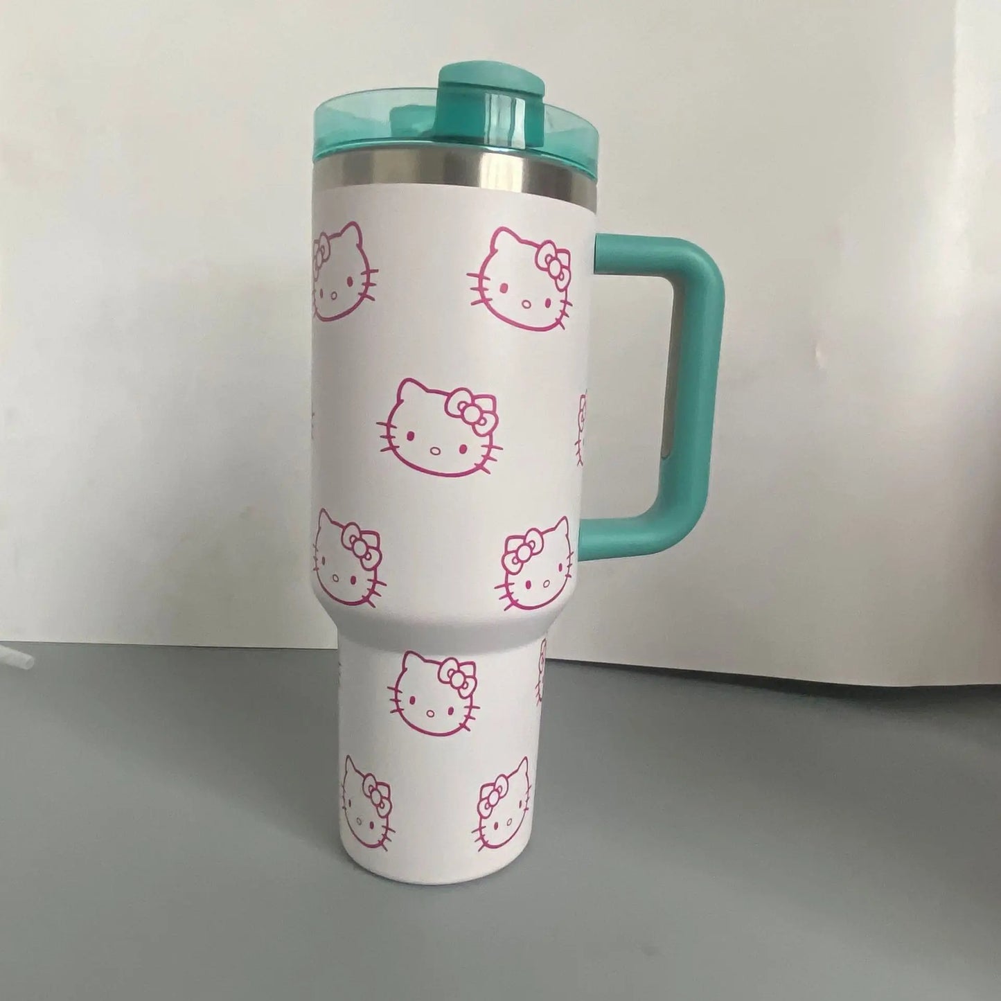 White tumbler with pink Hello Kitty faces and a teal handle and lid on a white background.