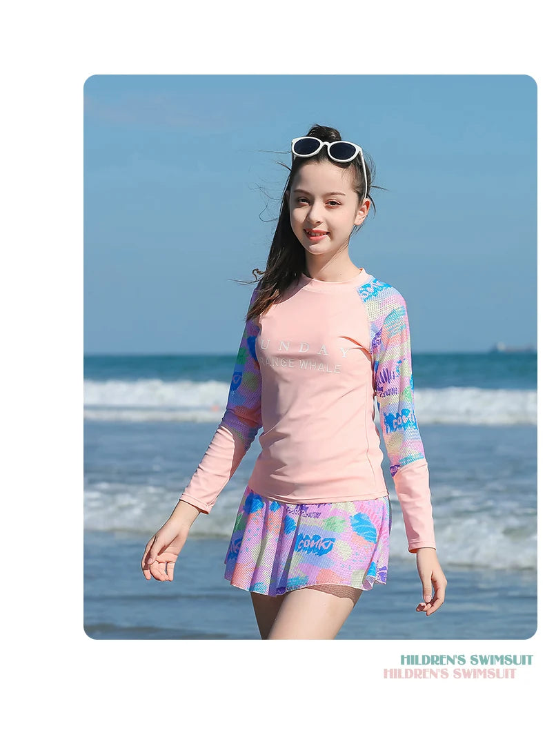 Young girl in a colorful swimsuit standing on a beach with ocean waves in the background.