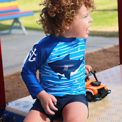 Child wearing a blue and white shark-patterned shirt sitting on a playground.